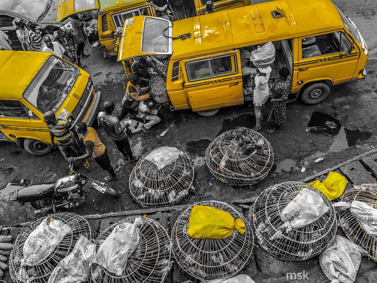 Overhead shot of yellow danfo buses and chicken cages at a Lagos market, everything else in grey